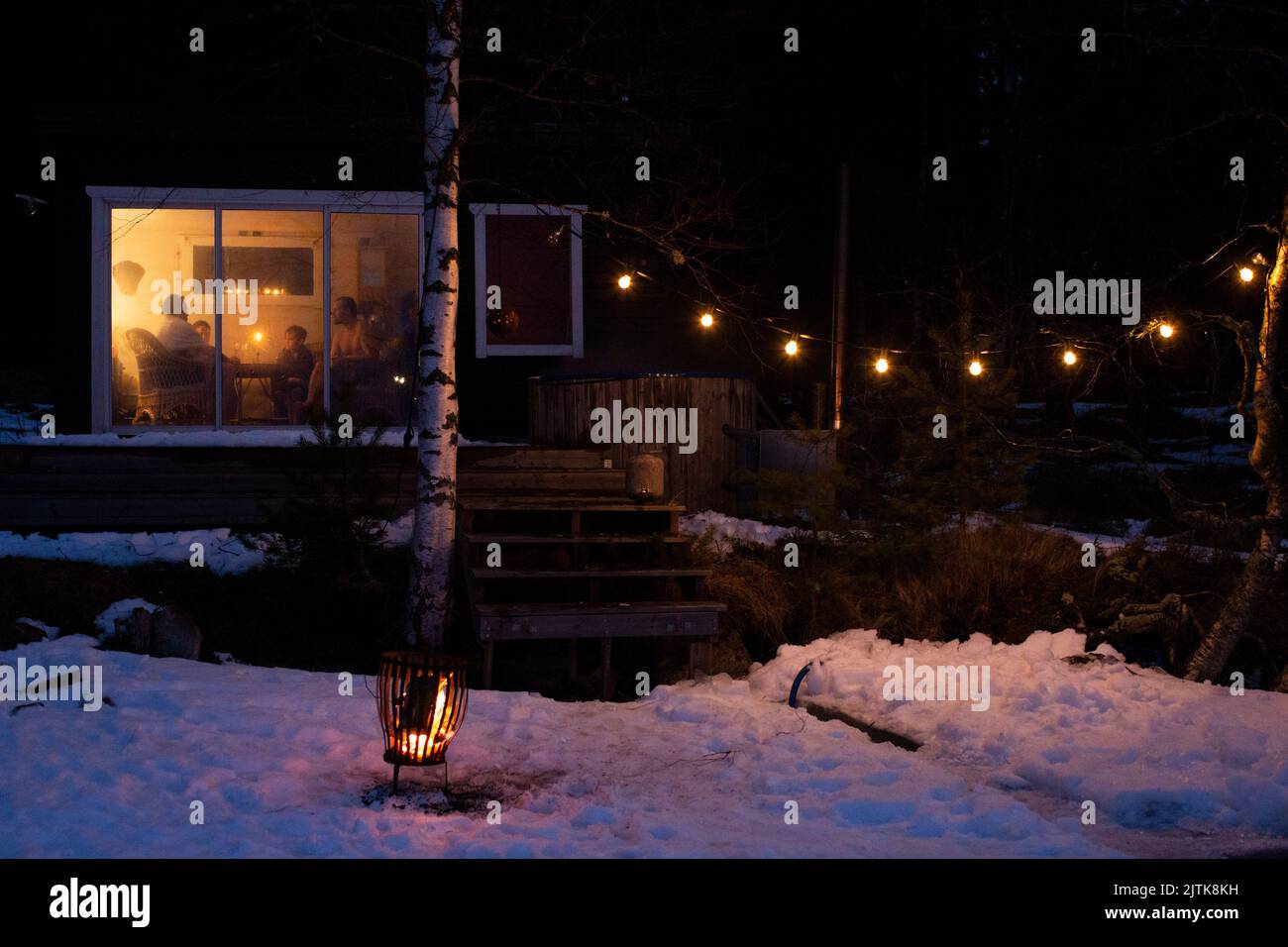 Uomini maturi con figli visti attraverso la finestra di casa illuminata in inverno di notte Foto Stock