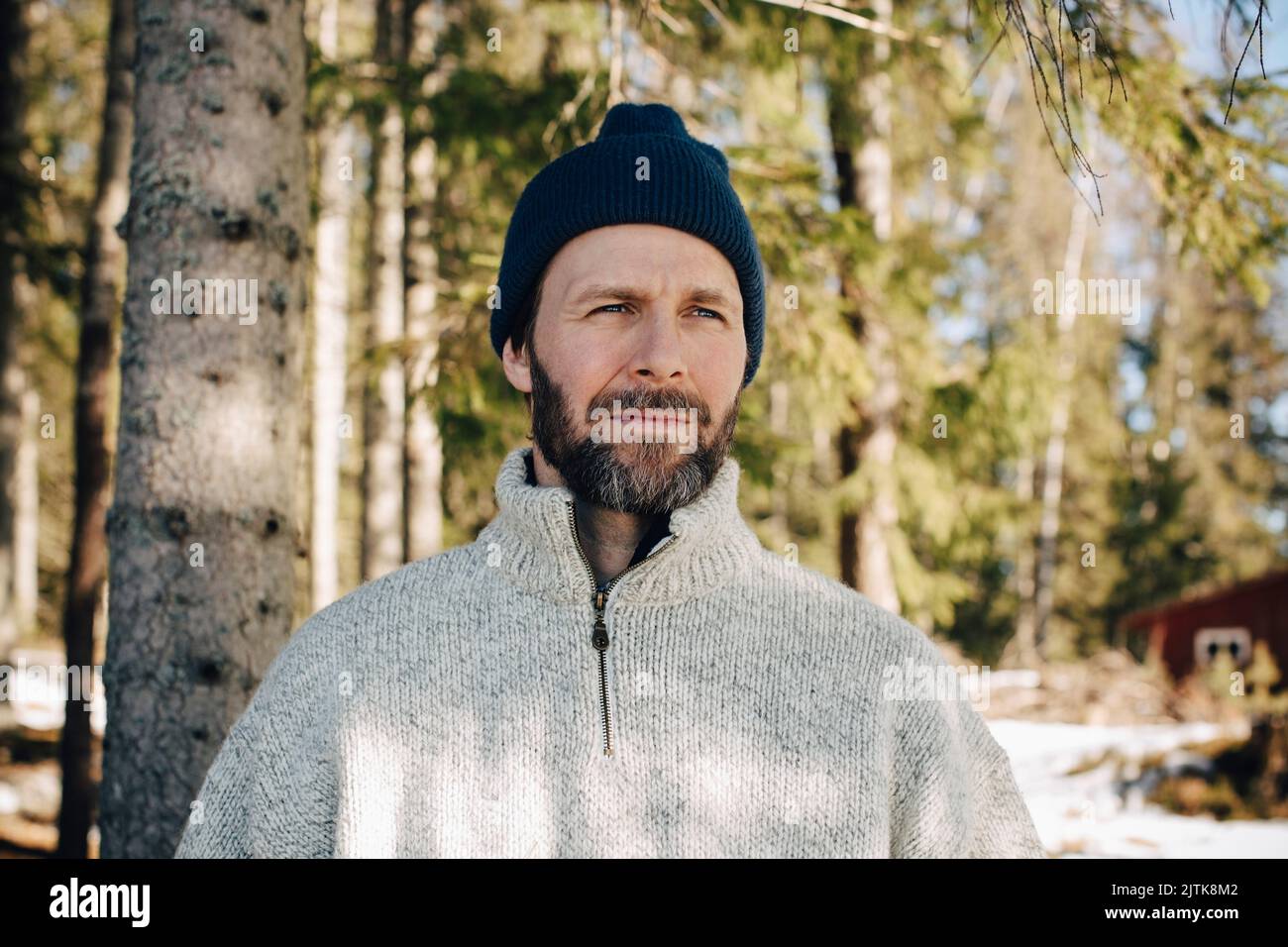 Uomo maturo che indossa un cappello a maglia che guarda lontano nella foresta Foto Stock