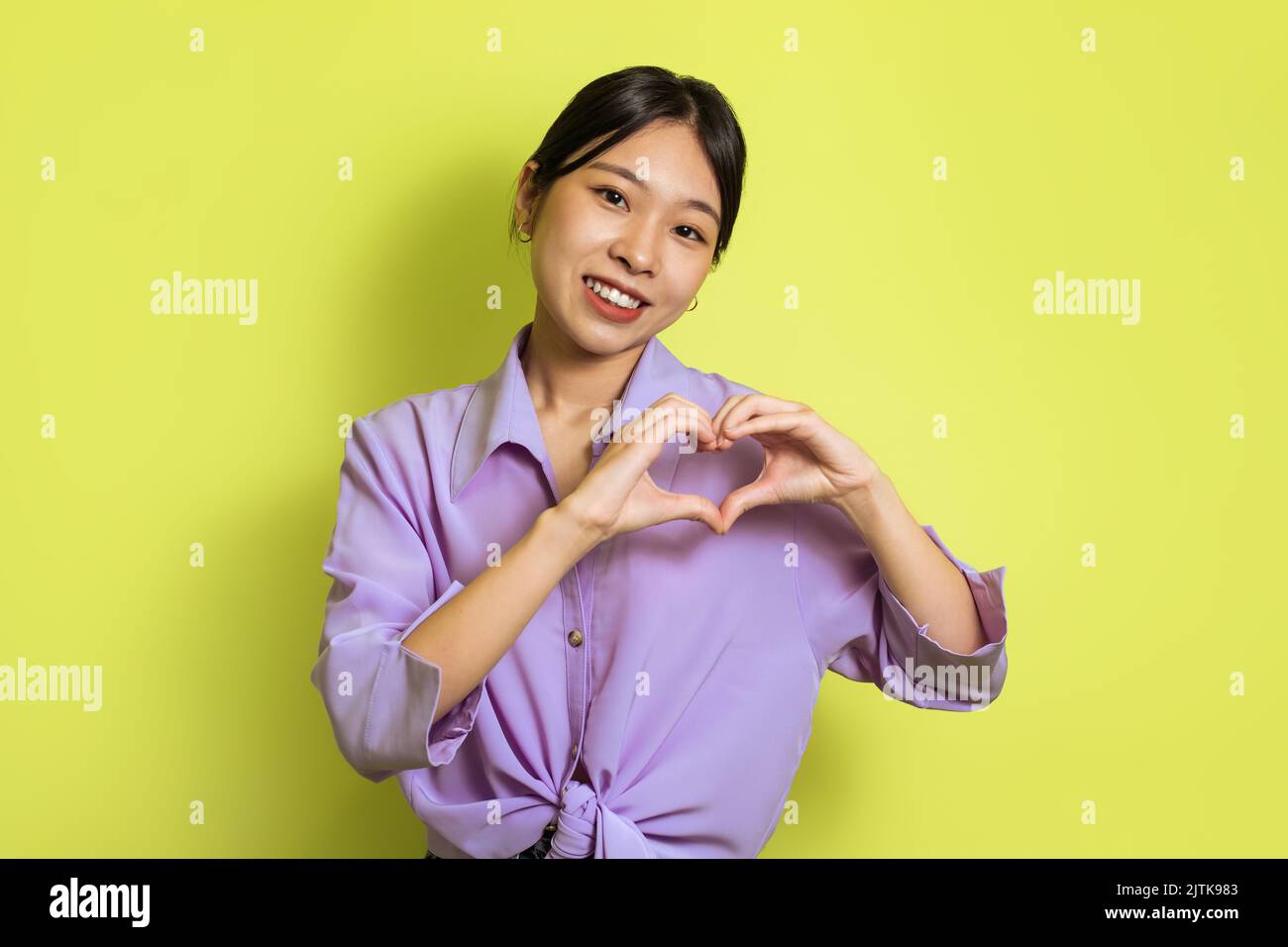 Donna coreana allegra mostrando dita cuore Gesture su sfondo giallo Foto Stock