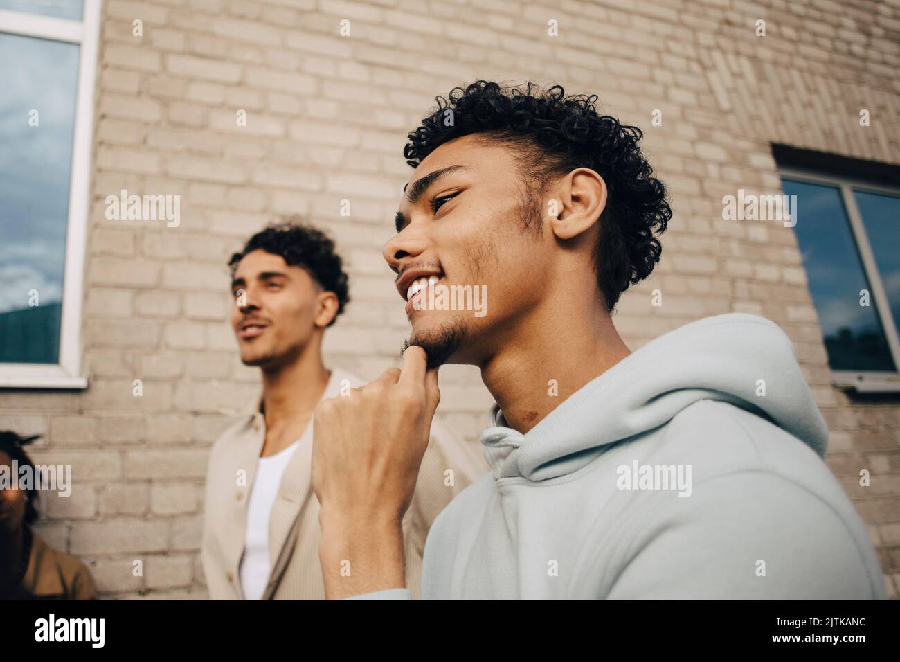 Uomo sorridente con la mano sul mento in piedi da un amico fuori edificio Foto Stock