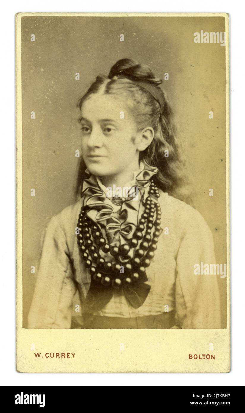 Originale ritratto in studio di una ragazza vittoriana adolescente, con lunghi capelli ondulati sciolti, della CDV vittoriana (carte de visite o Visiting card) ma legata dal viso, indossa una camicetta con un ruff e una spilla frontali e diversi splendidi anelli di perline che sono probabilmente fatti di jet (vedi la principessa Louise Duchessa Argyll, che indossa perline simili in un ritratto datato 1870). Dallo studio di W. Currey, Bark Street, Bolton, Lancashire, Inghilterra, Regno Unito all'inizio degli anni '1870 Foto Stock