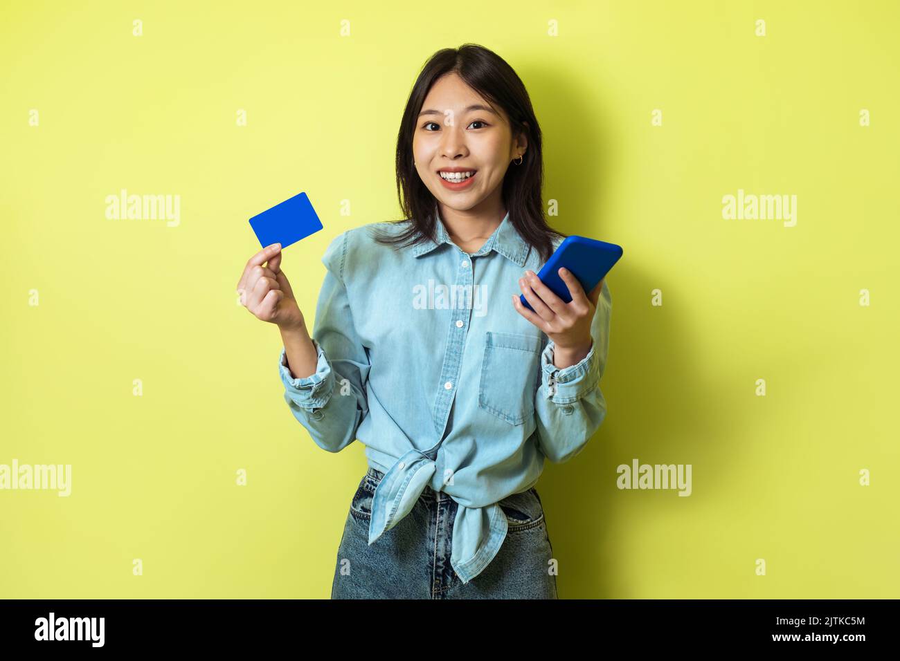 Asian Woman Shopping Holding carta di credito e telefono, sfondo giallo Foto Stock