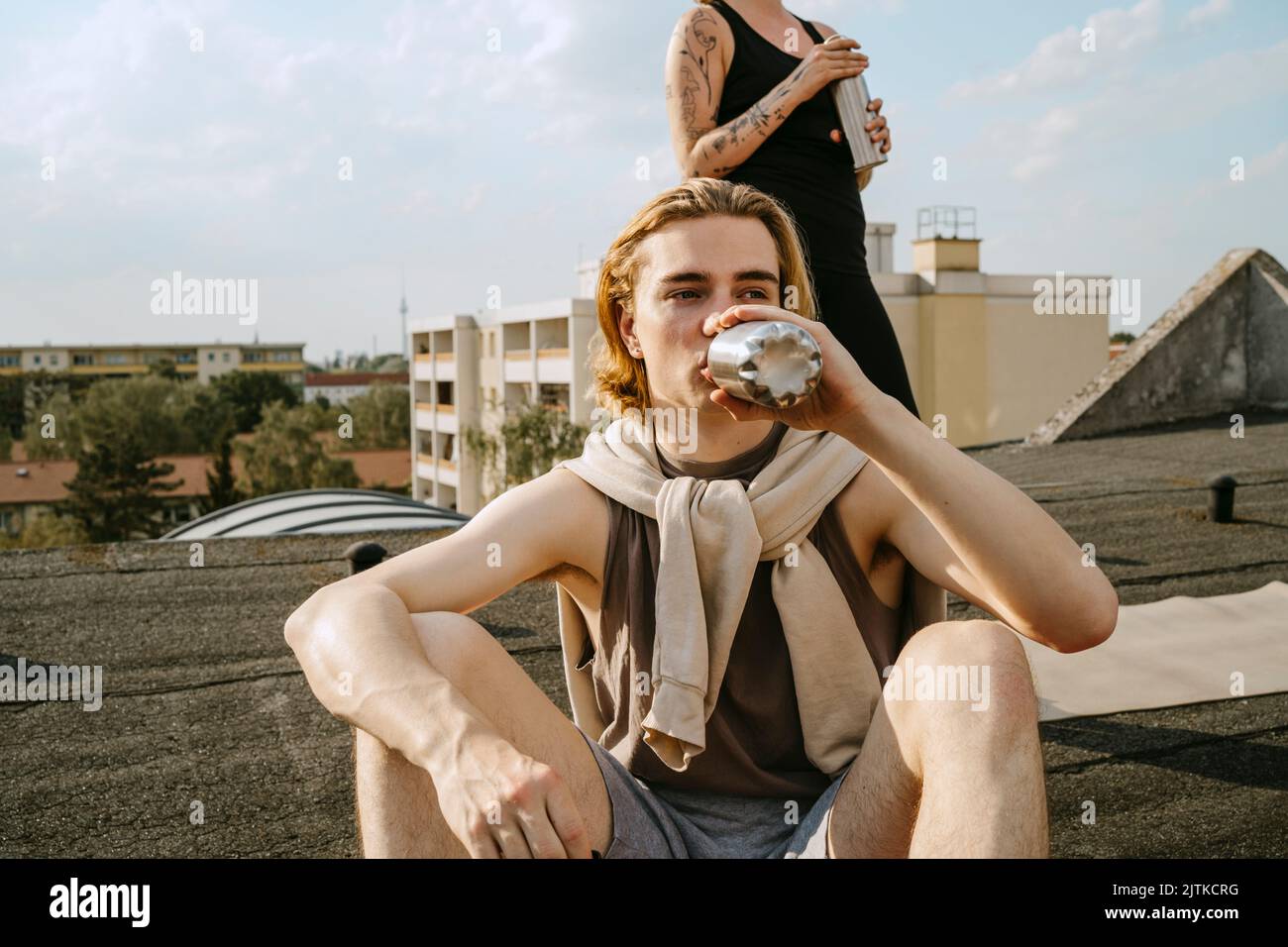 Un giovane uomo che beve acqua seduto di fronte ad un amico sul tetto Foto Stock