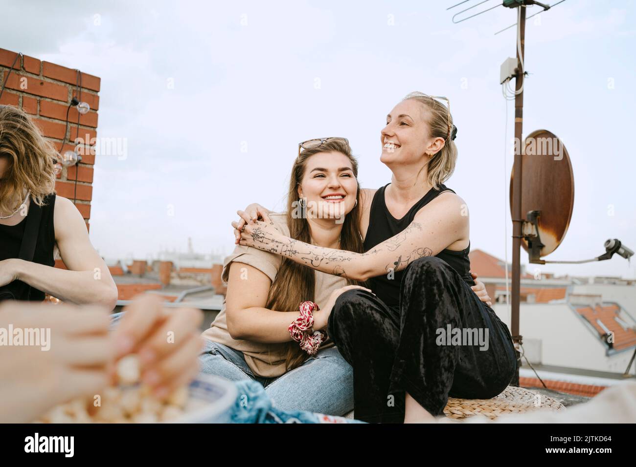 Donna felice seduta braccio intorno con l'amico femmina sul tetto Foto Stock