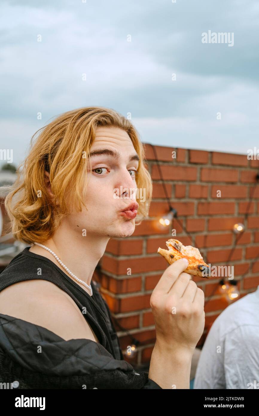 Ritratto di giovane biondo con labbra puckering pizza sul tetto Foto Stock