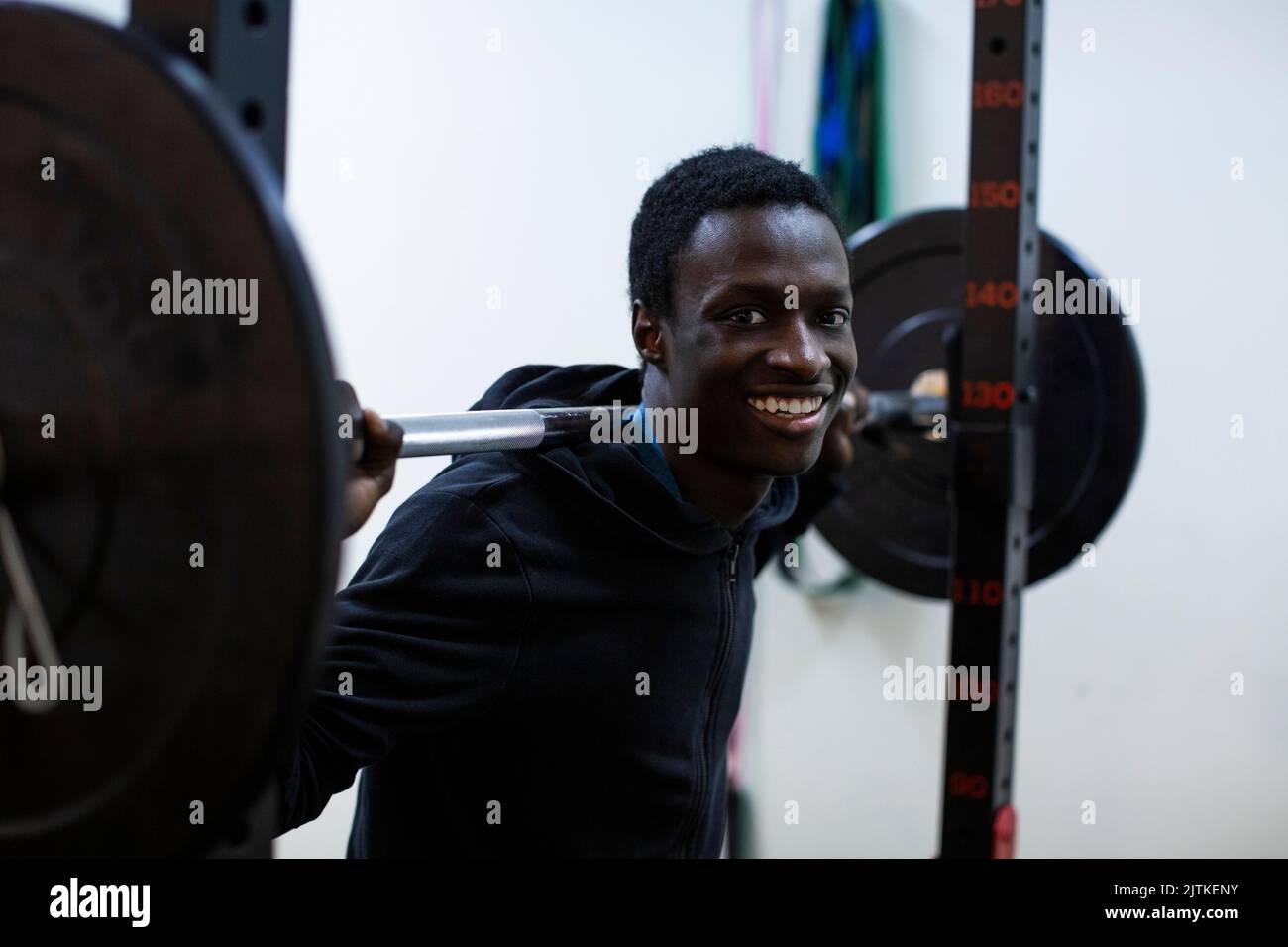 Ritratto di atleta sorridente che porta il barbell sulla spalla in palestra Foto Stock