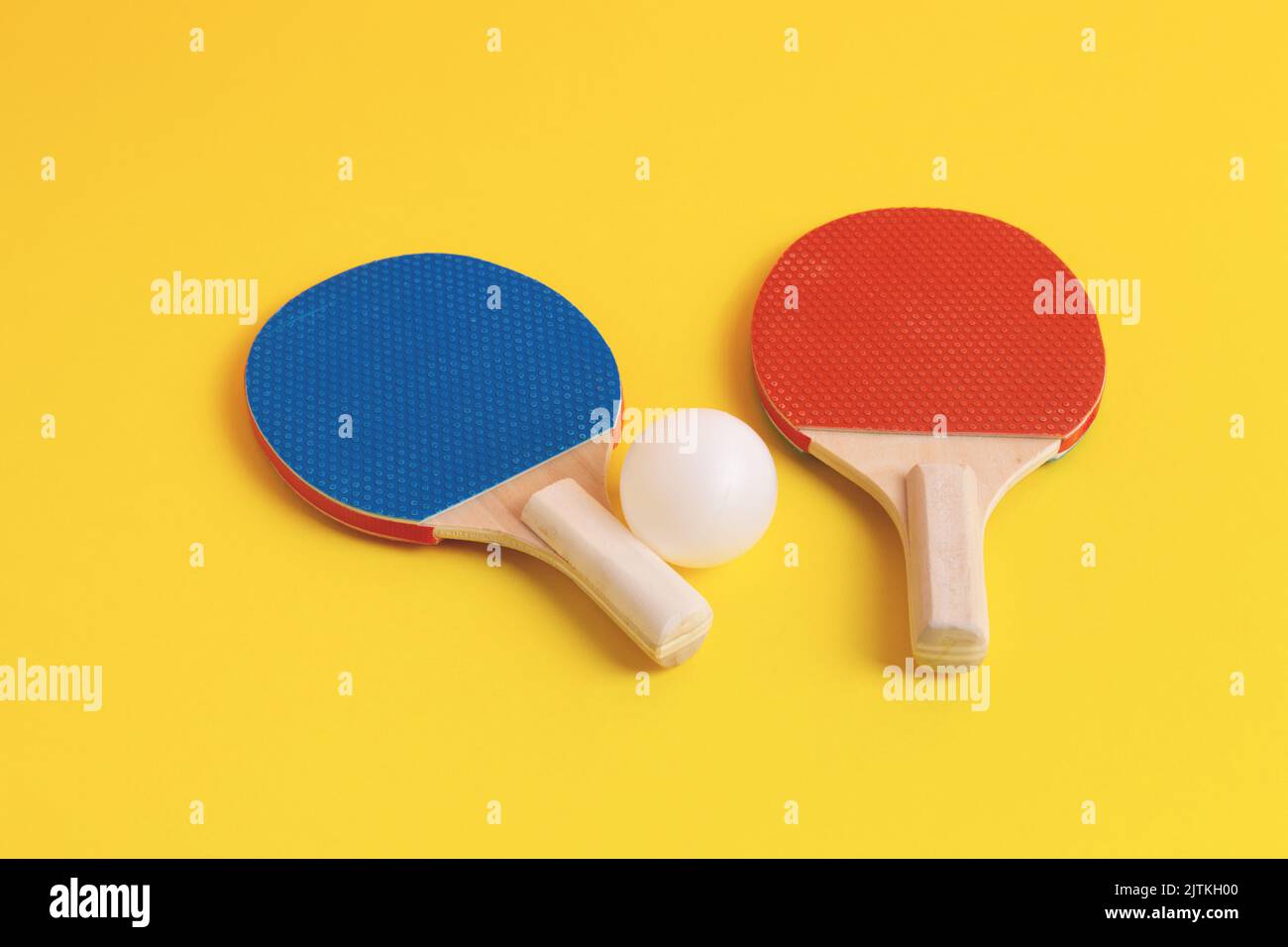 Racchette da ping pong e palla bianca su sfondo giallo. Attrezzatura sportiva. Foto Stock