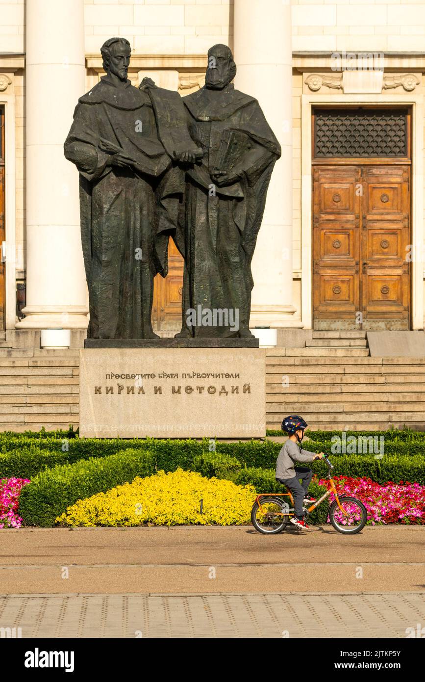 La Biblioteca Nazionale e un bambino in bicicletta presso la statua dei fratelli Cirillo e Metodio a Sofia, Bulgaria, Europa orientale, Balcani, UE Foto Stock