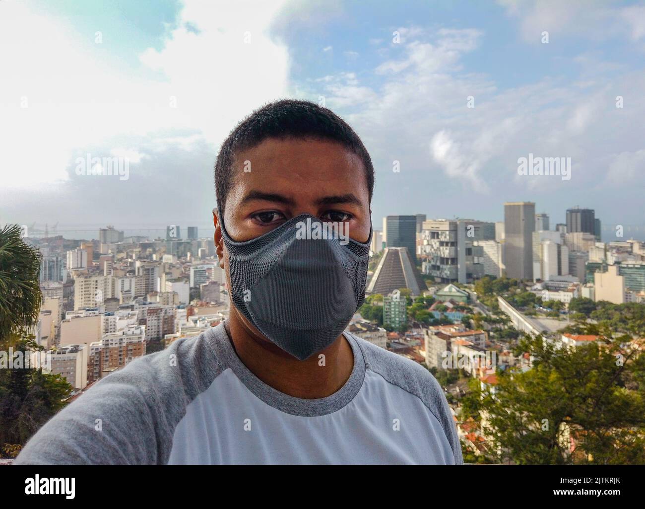 Uomo nero che indossa una maschera con il centro di Rio de Janeiro sullo sfondo, durante la pandemia del coronavirus in Brasile. Foto Stock