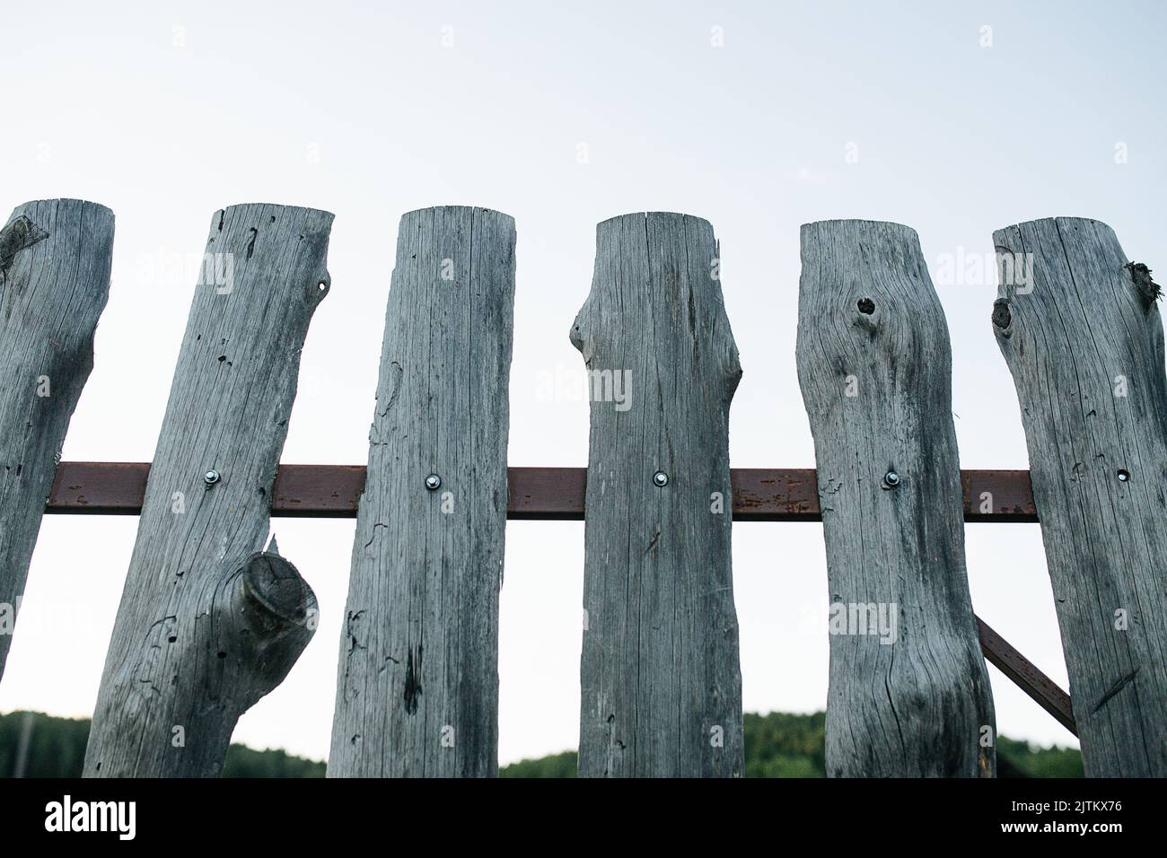 Angolo verso l'alto di legno vecchio a buon mercato struttura di recinzione di lastra su un telaio di metallo da tavole rotonde annodate con ampi spazi pari in mezzo. Foto Stock
