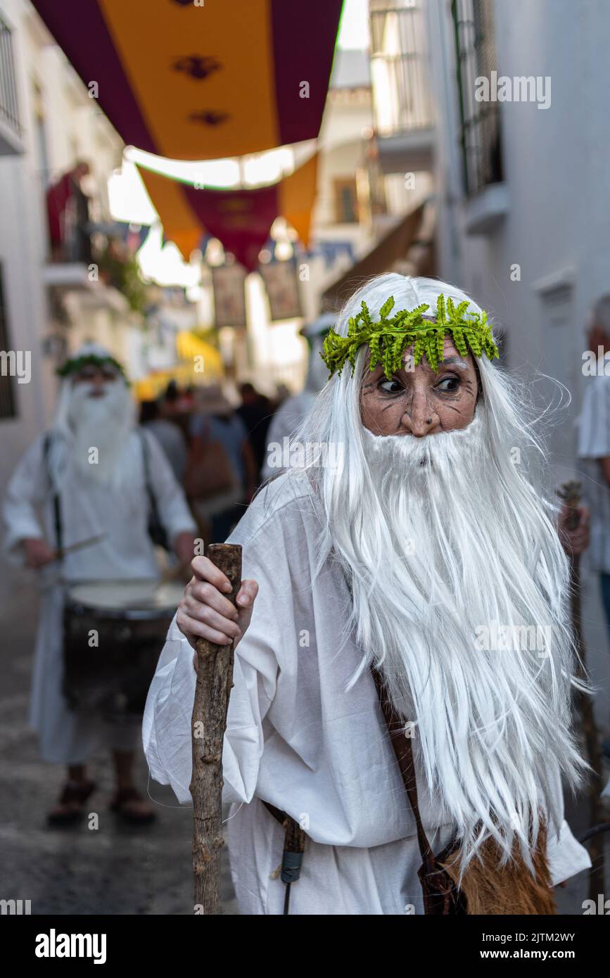 Frigiliana, Malaga, Spagna, 27 agosto 2022: Druid vestito di bianco con un ramo d'albero come un bastone con una fascia di foglie verdi nelle strade di Frigg Foto Stock