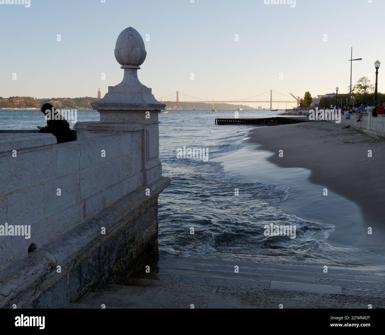 Zona murata con colonne e gradini che conducono alla spiaggia sul fiume Tago con il ponte 25 de Abril alle spalle. Lisbona, Portogallo Foto Stock