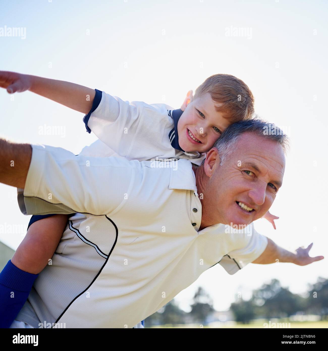 Dare le ali della sua immaginazione. Ritratto di un padre che gioca con suo figlio sulla schiena fuori. Foto Stock