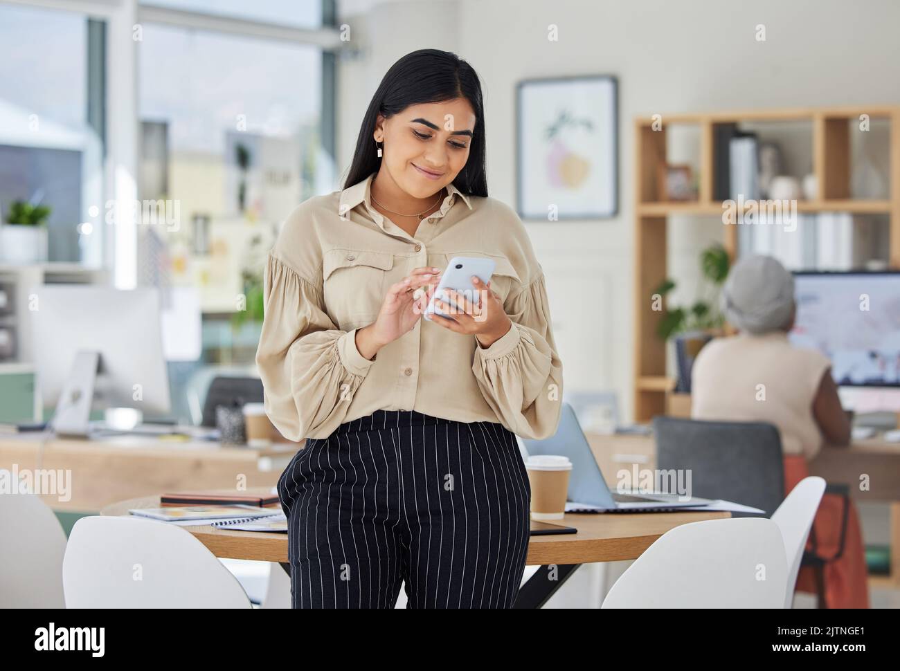 Imprenditore al telefono con social media online in un ufficio moderno. La donna d'affari sorride mentre chiacchiera e controlla l'e-mail al lavoro o condivide buone notizie Foto Stock