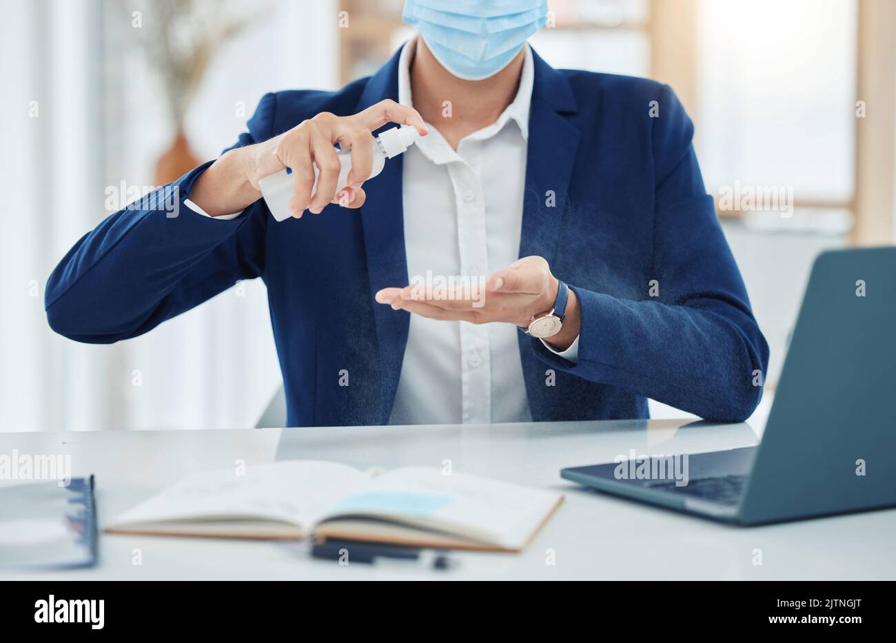 Uomo d'affari pulisce a spruzzo con una maschera covid mentre lavora in un ufficio. Imprenditore pulizia e disinfezione delle mani per prevenire la diffusione di Foto Stock