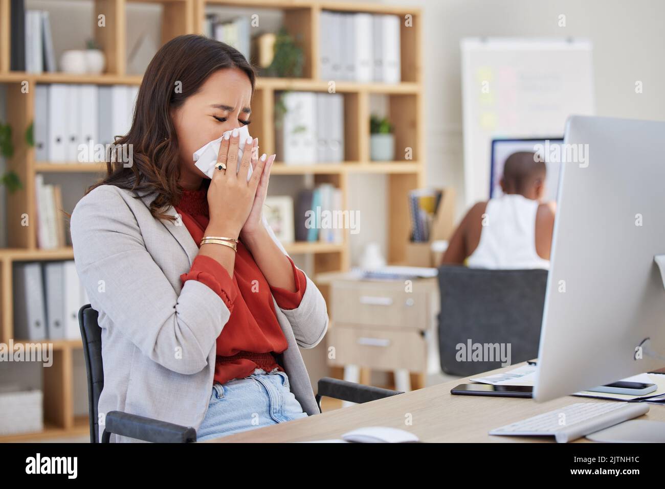 Donna d'affari malata, malata e starnutizzante con raffreddore, influenza o allergia mentre lavora in ufficio. Workaholic o manager che cerca di lavorare alla scrivania con covid Foto Stock