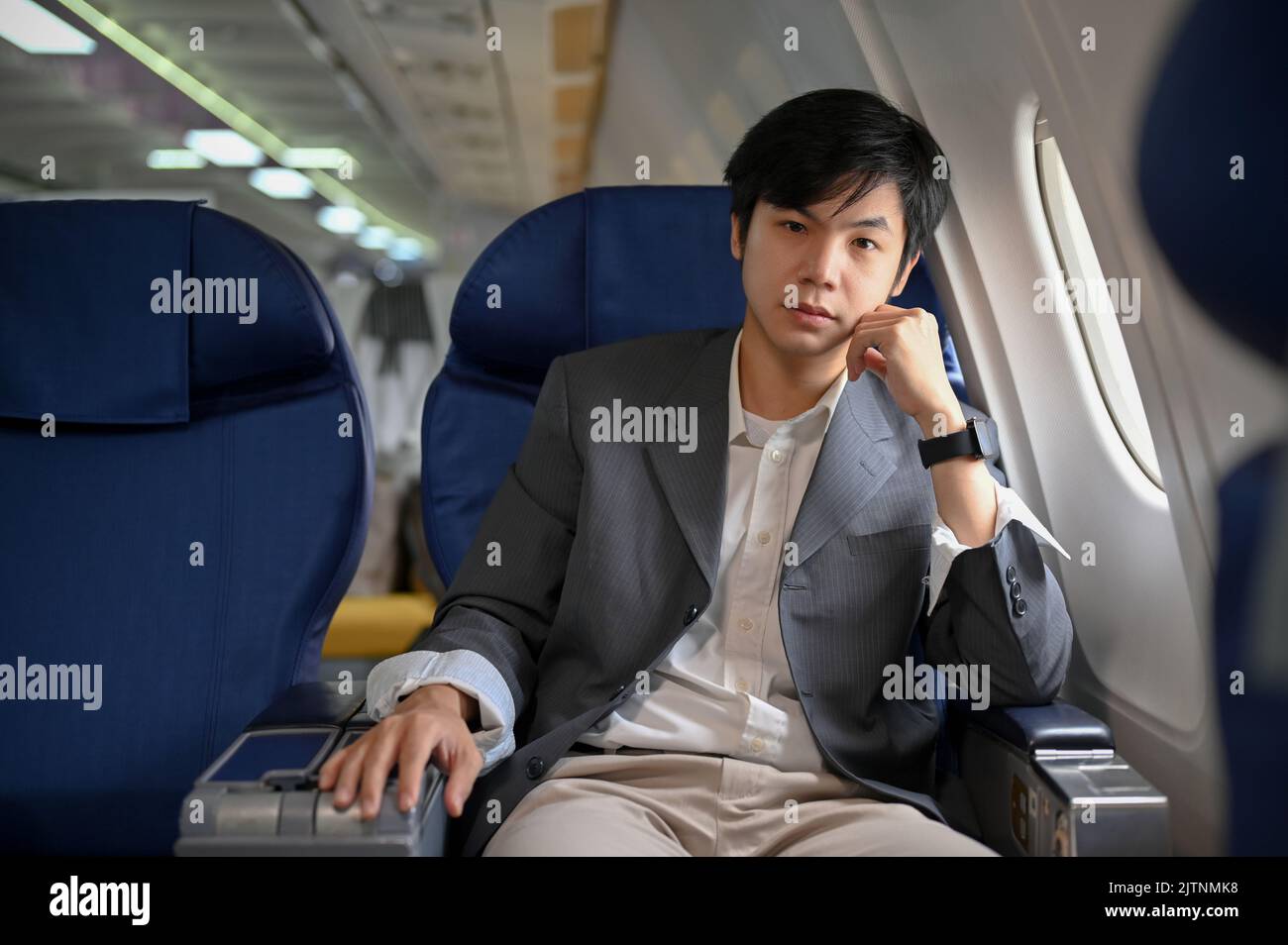 Bell'uomo d'affari asiatico e giovane astuto o capo d'affari in abito formale siede al posto della finestra in una classe business. Trasporto aereo concep Foto Stock