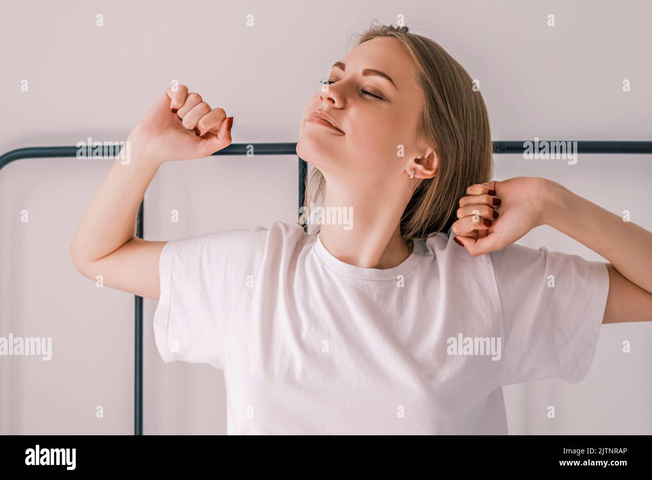 Svegliati al mattino. Giovane donna addormentata si allunga a letto con gli occhi chiusi, diffondendo i gomiti in direzioni diverse mentre si siede dentro Foto Stock