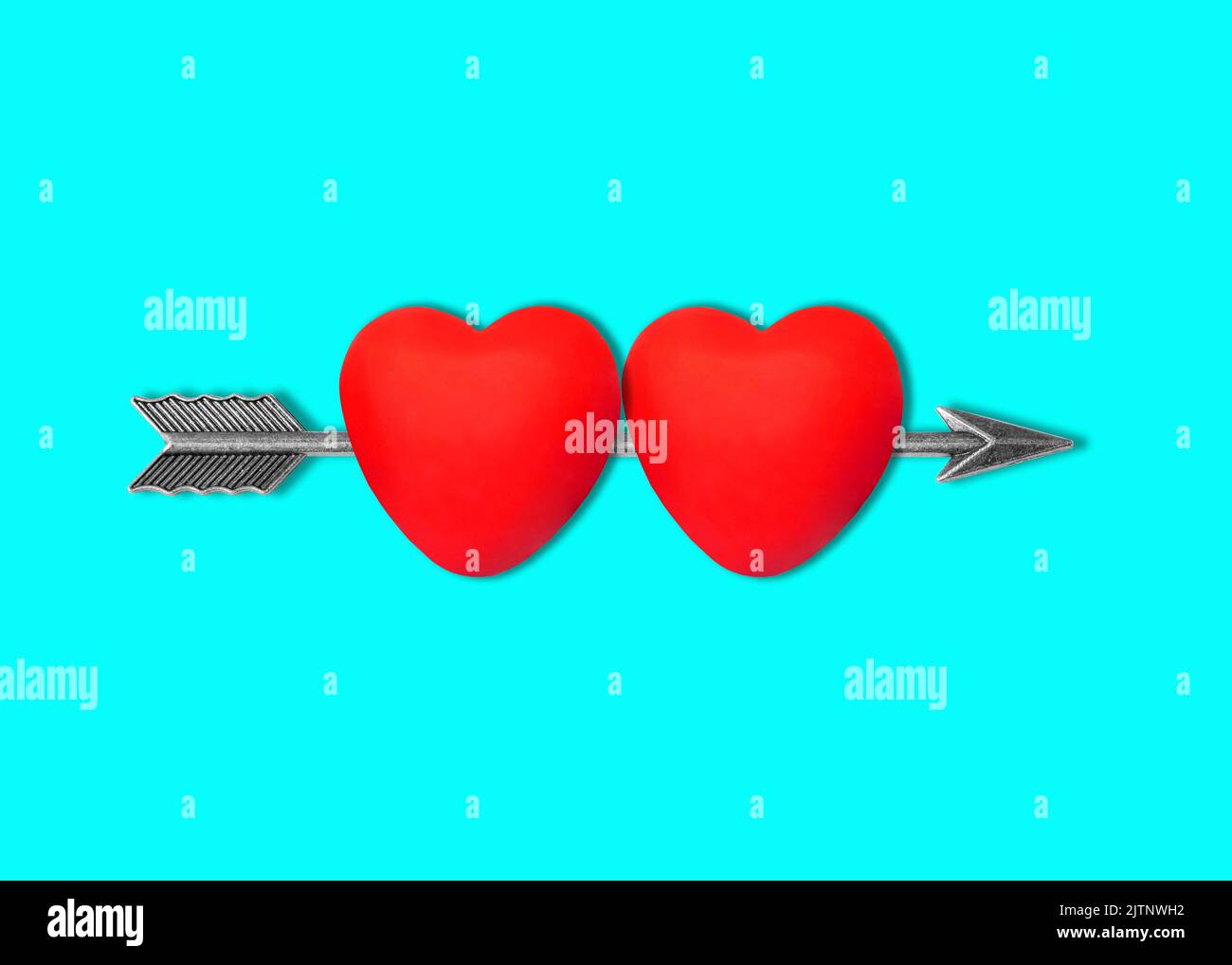 Due forme di cuore trafitto da una freccia di arco in acciaio isolata su sfondo blu. Foto Stock
