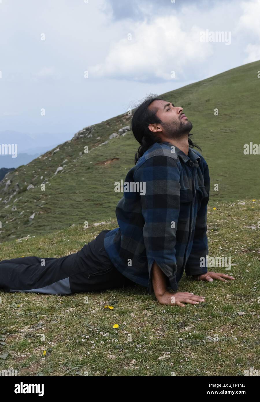 Un bel giovane indiano dai capelli lunghi che fa posa Cobra (posa Bhujangasana Yoga) in montagna Foto Stock
