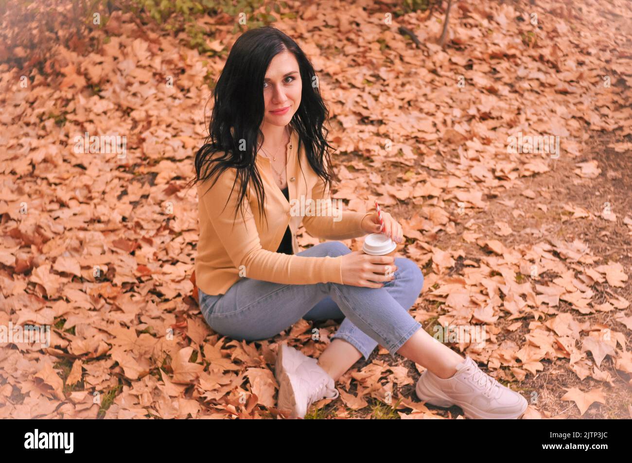 Donna brunetta in t-shirt gialla jeans blu snd seduta su foglie arancioni in autunno Foto Stock