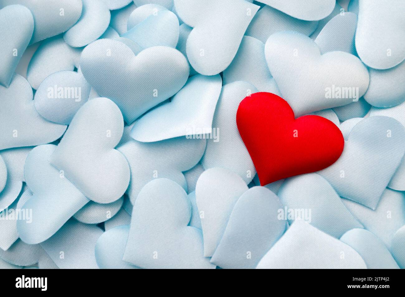 Un singolo cuore tessile rosso su cuori blu pastello multipli con concetto di spazio copia per il legame tra gli amanti, relazioni romantiche e romanticismo backgro Foto Stock