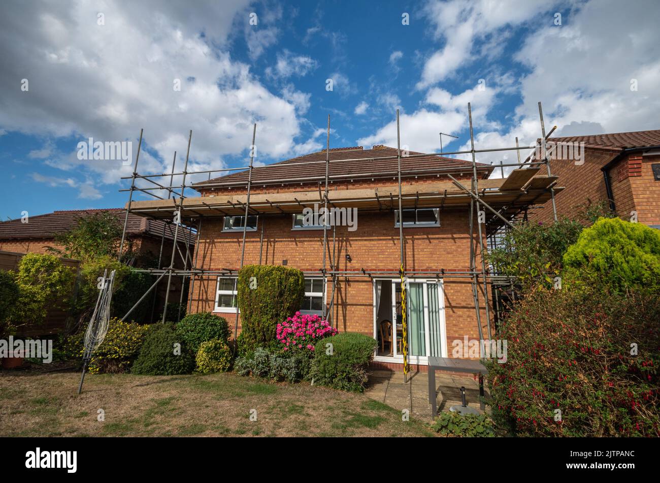 Casa indipendente in mattoni rossi degli anni '90 con impalcature erette per consentire la riparazione del tetto; Wootton, Northampton, Regno Unito Foto Stock