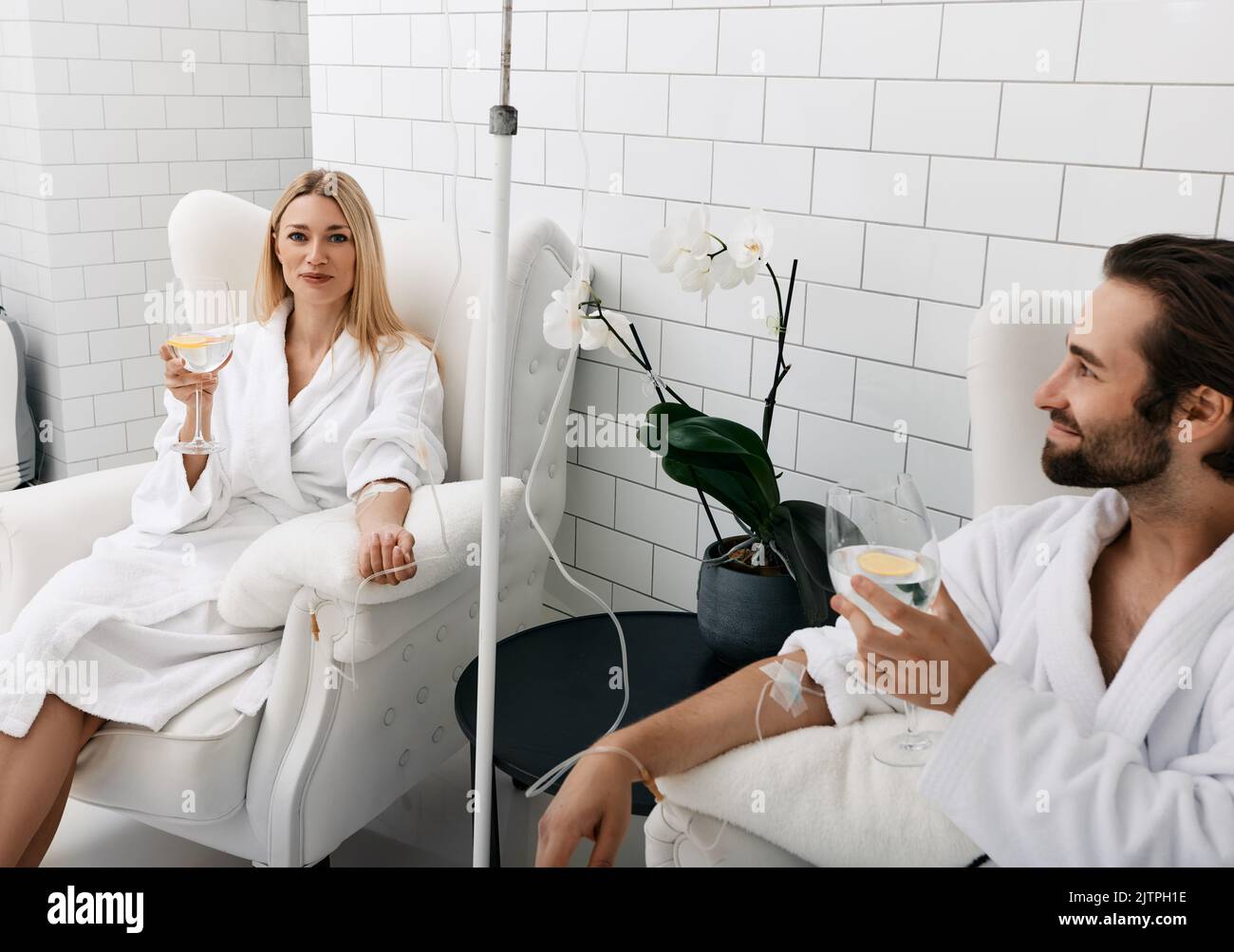 Coppia innamorata durante la terapia endovenosa della vitamina. Bella donna con il suo ragazzo con bicchieri di bevanda rinfrescante al limone in clinica medica fo Foto Stock