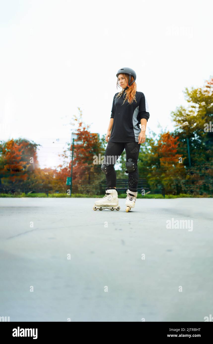 Giovane donna con pattini a rotelle in piedi in un parco di pattini durante un primo giorno di autunno Foto Stock