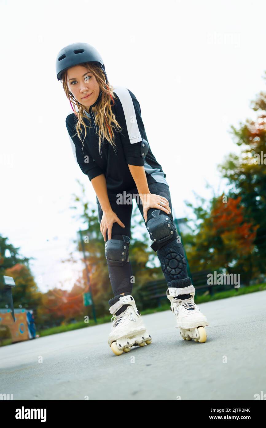 Giovane donna con le lame a rotelle che si diverse la sua giornata autunnale in un parco di skate cittadino Foto Stock