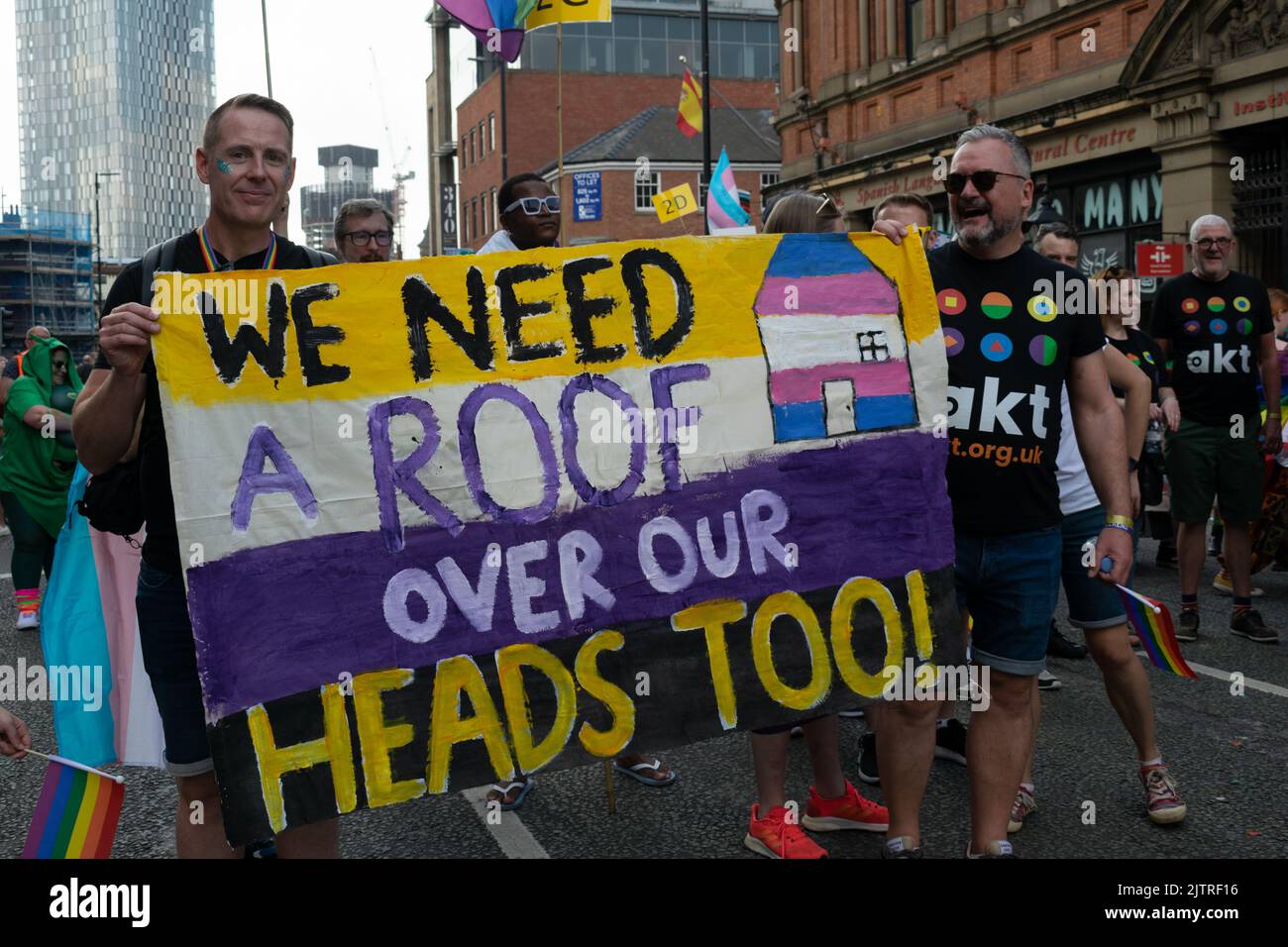 Sfilata del Manchester Pride. AKT beneficenza senza tetto marciando con banner testo abbiamo bisogno di un tetto sopra le nostre teste troppo. Marcia tematica per la Pace. Foto Stock