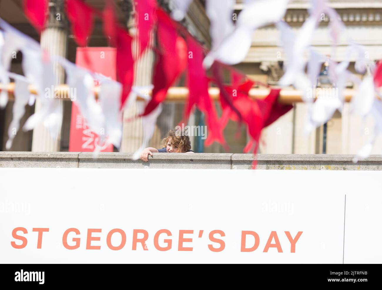 Uno spettatore è visto dietro le decorazioni mentre le persone si riuniscono per le celebrazioni del giorno di San Giorgio a Trafalgar Square, nel centro di Londra. Foto Stock