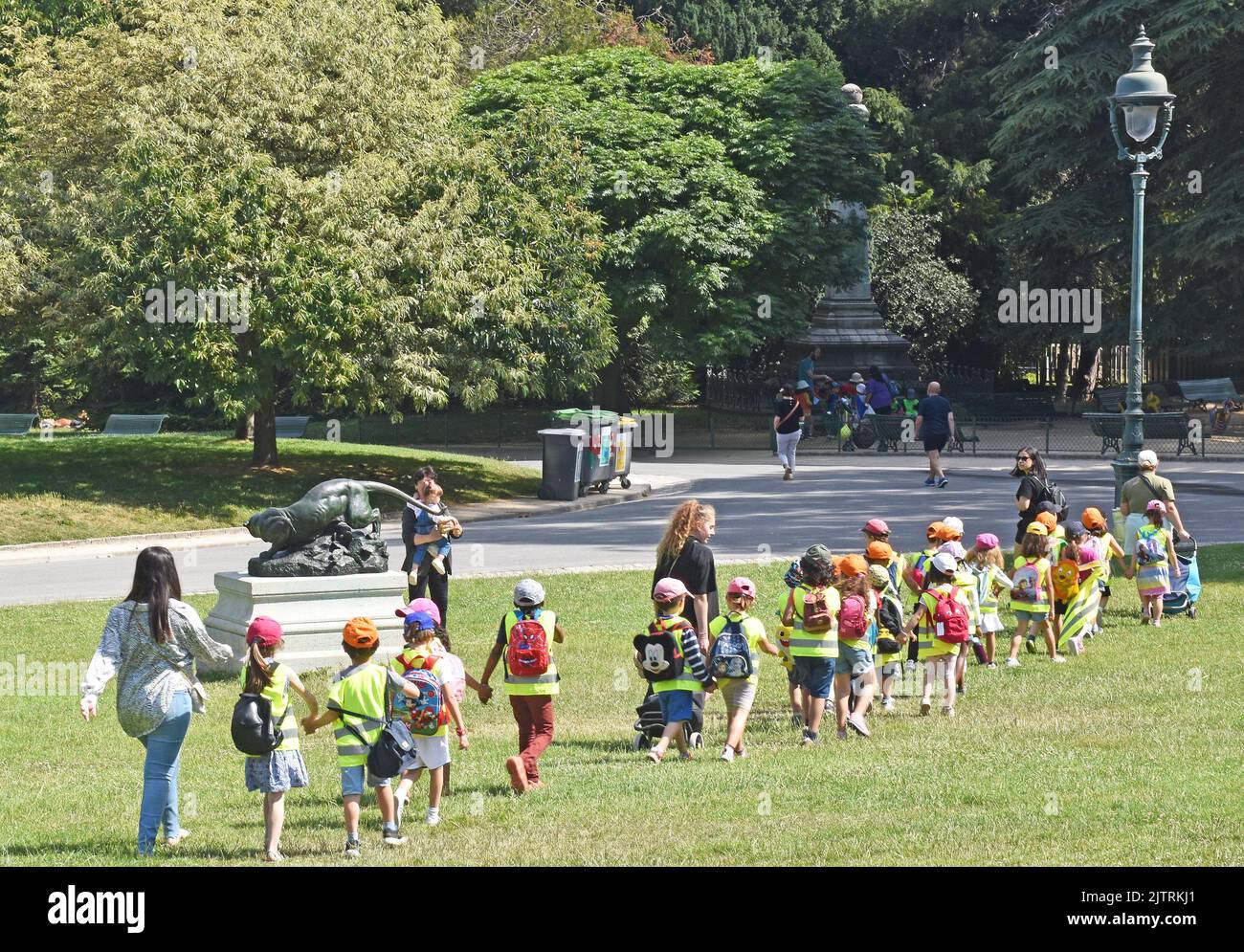 Una classe di bambini piccoli che vengono pastorati attraverso Parc Montsouris, Parigi, in coppie, tutti tenendo le mani, e indossando dorature hi-vis e berretti da baseball Foto Stock