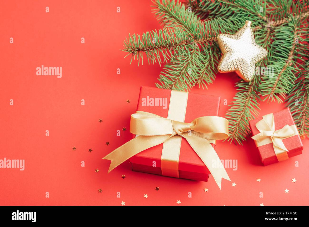 Piatto natalizio con scatole regalo rosse e rami di abete, confetti dorati su sfondo rosso. Vista dall'alto, spazio di copia. Foto Stock