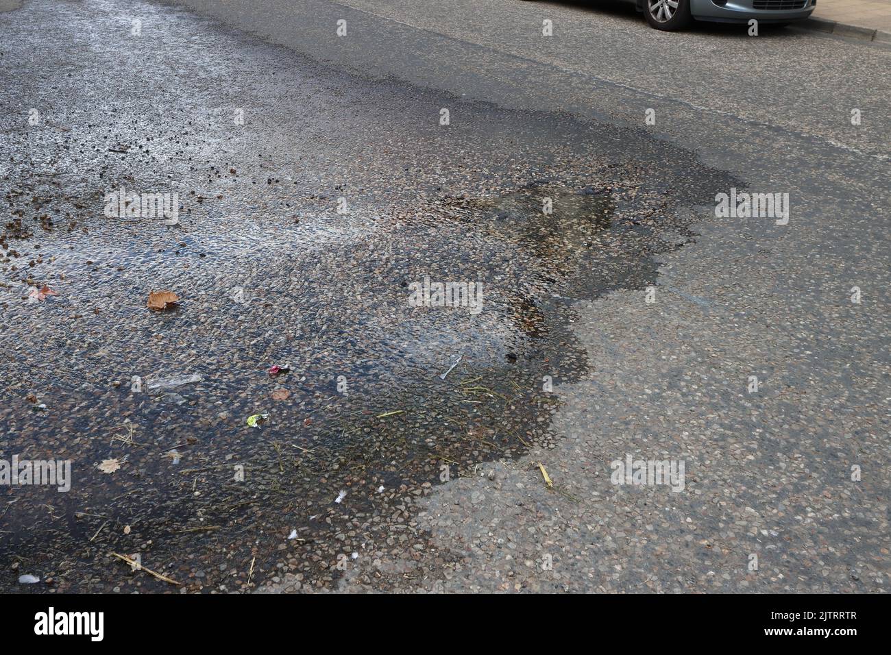 L'acqua proveniente da un tubo sotterraneo scappa attraverso la superficie stradale di Broad Street, Boxford, Suffolk, UK Foto Stock