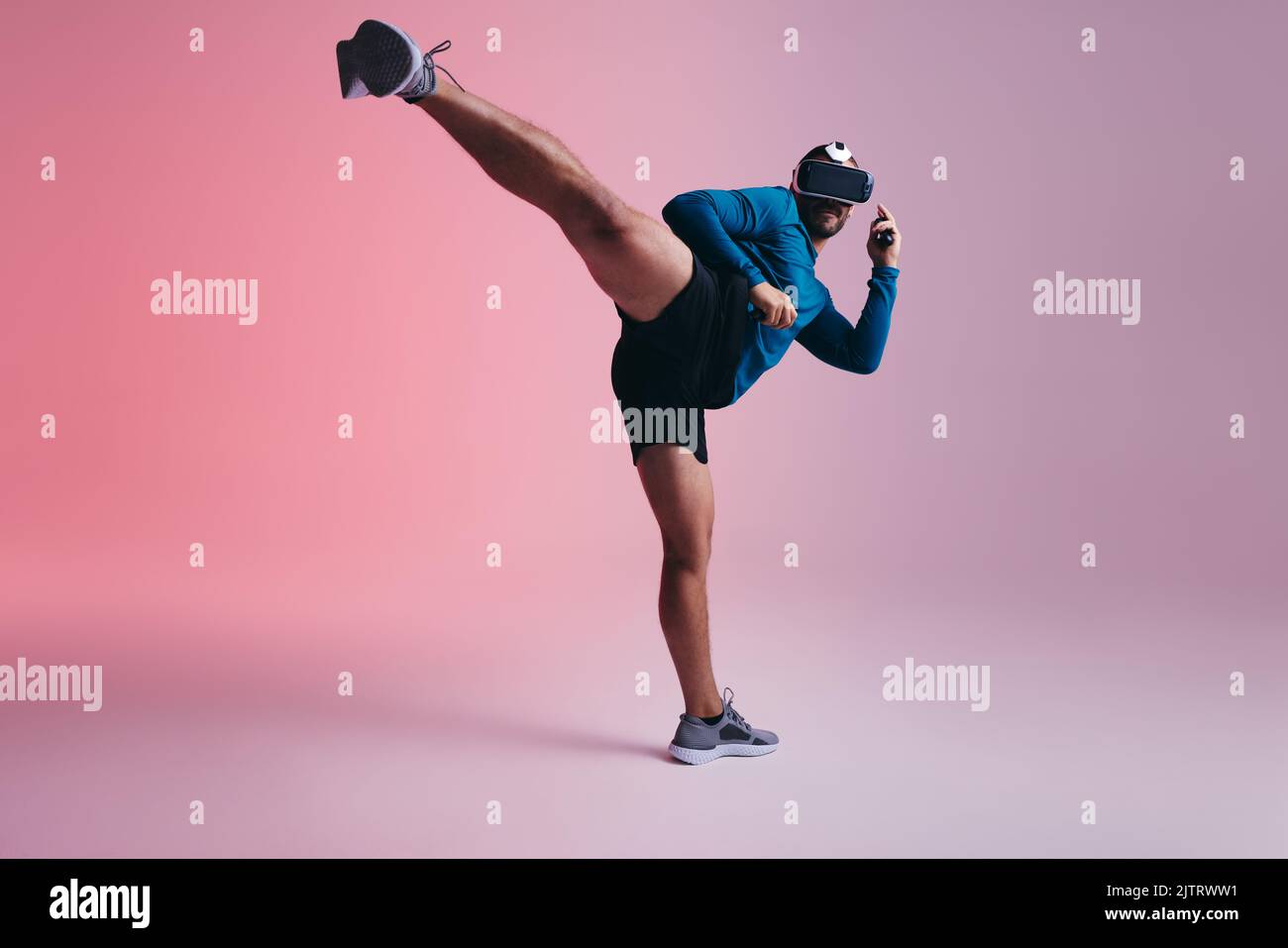 Giovane attivo che pratica le arti marziali nel metaverse. Giovane sportivo che lancia un calcio a mezz'aria indossando occhiali per realtà virtuale. Giovane e Foto Stock