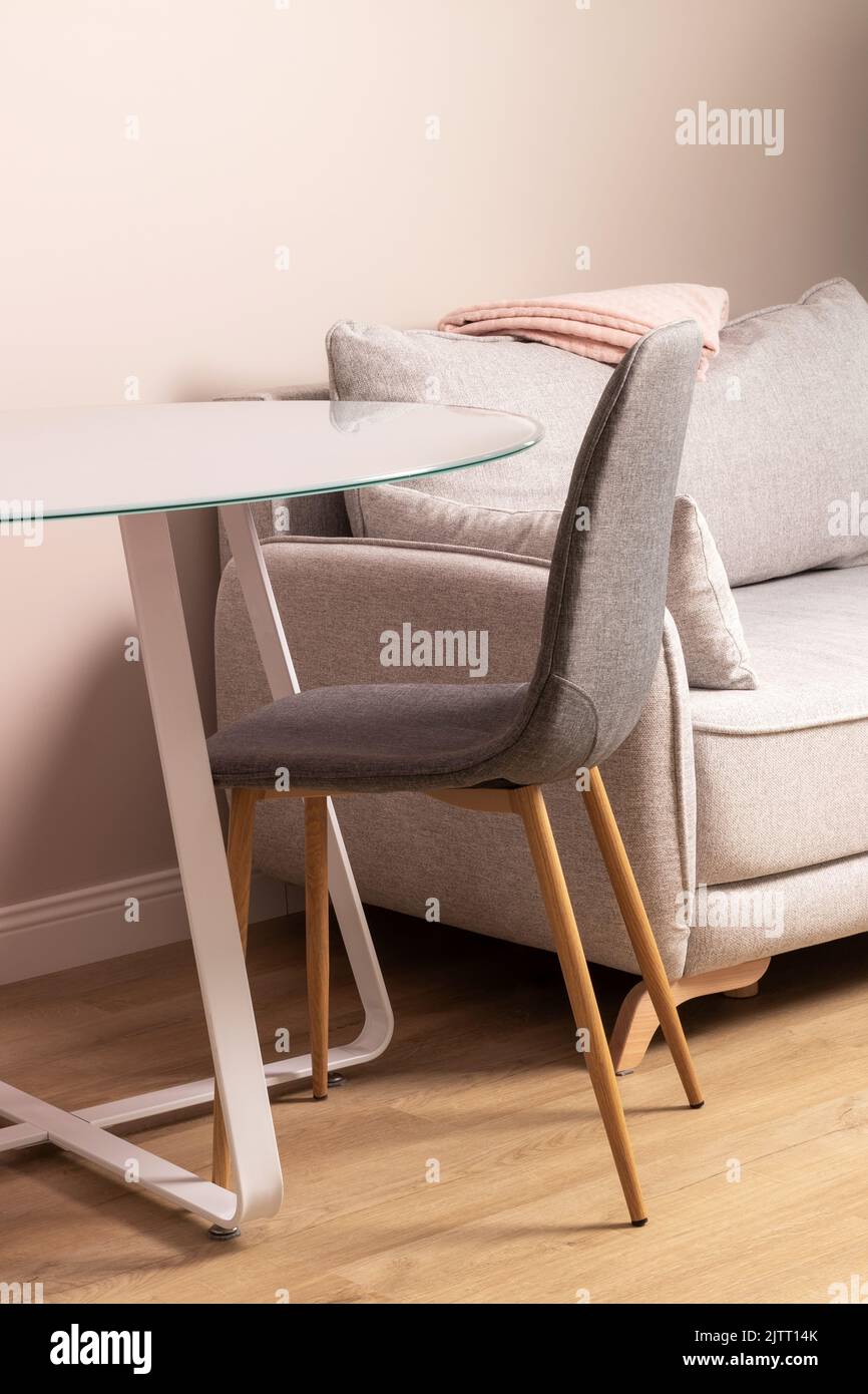 Tavolo in vetro, sedia in tessuto, divano grigio con plaid rosa ripiegato. Moderno soggiorno o cucina closeup Foto Stock