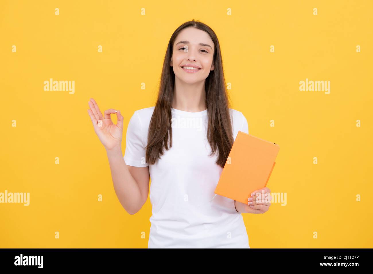 Giovane studentessa in abiti casual, isolata su sfondo giallo studio ritratto. Tenere i notebook. Giovane ragazza allegra e attraente studentessa. Foto Stock