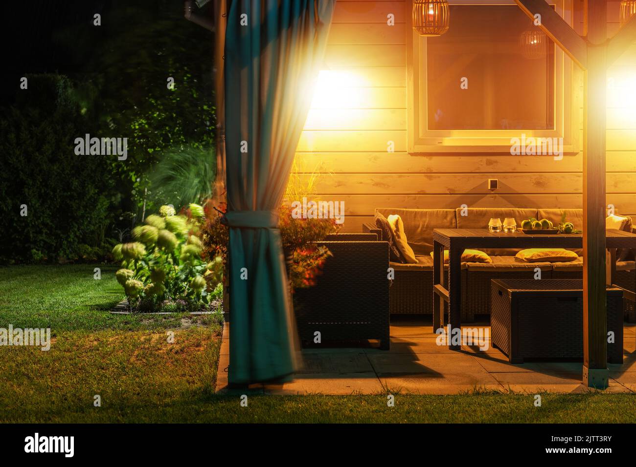 Terrazza nel giardino del cortile della famiglia Living House arredato per pranzare con mobili da esterno. Atmosfera intima serale con luci calde accese e. Foto Stock