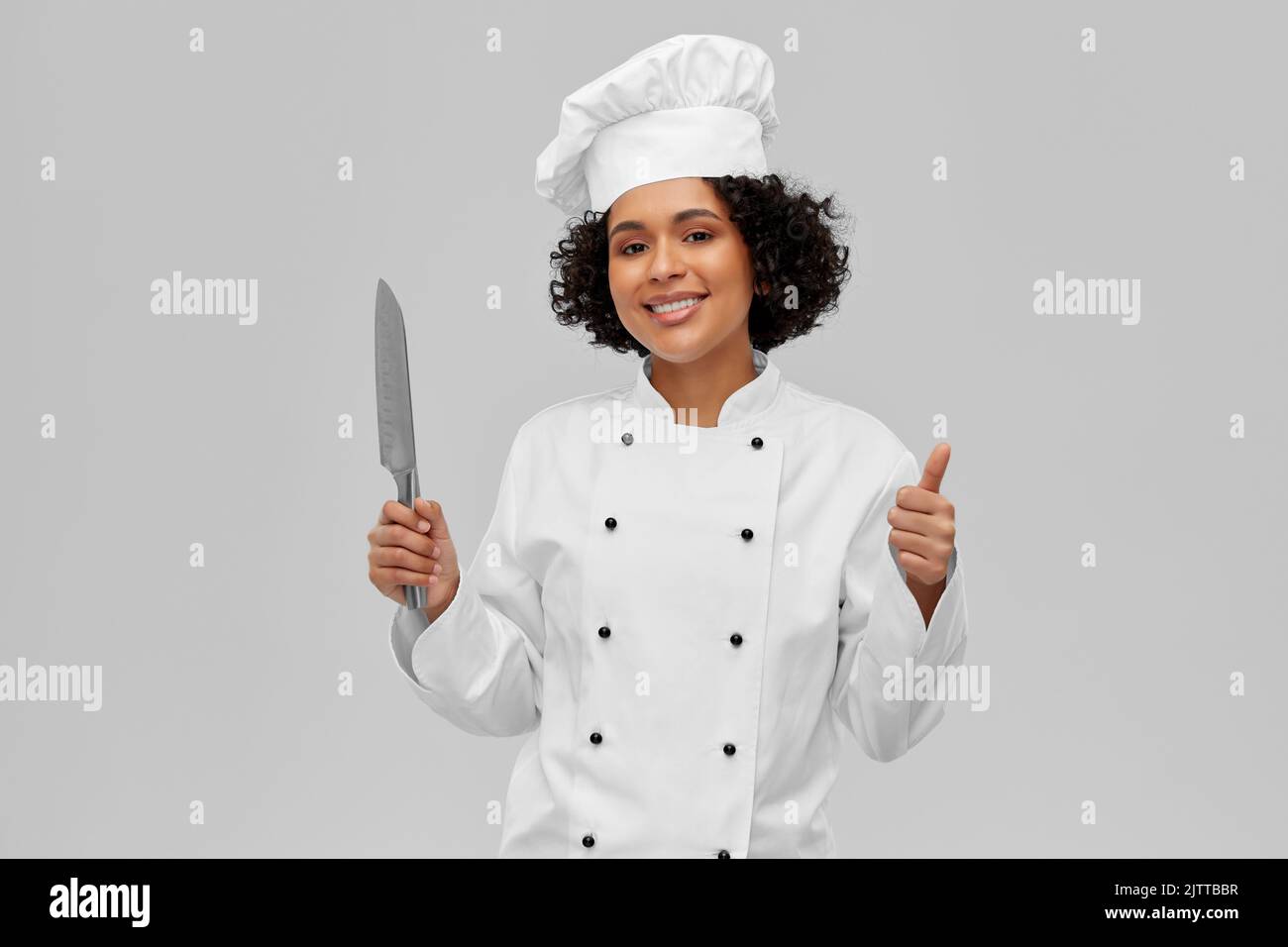 cuoco femminile in toque con coltello che mostra i pollici in su Foto Stock