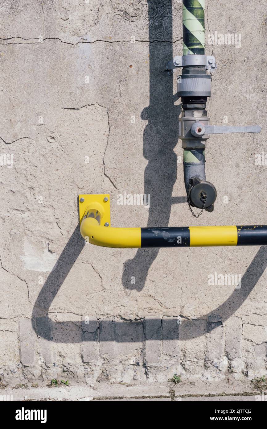 Tubo di una stazione di pompaggio e barra di sicurezza in giallo nero su una parete di cemento. Foto Stock