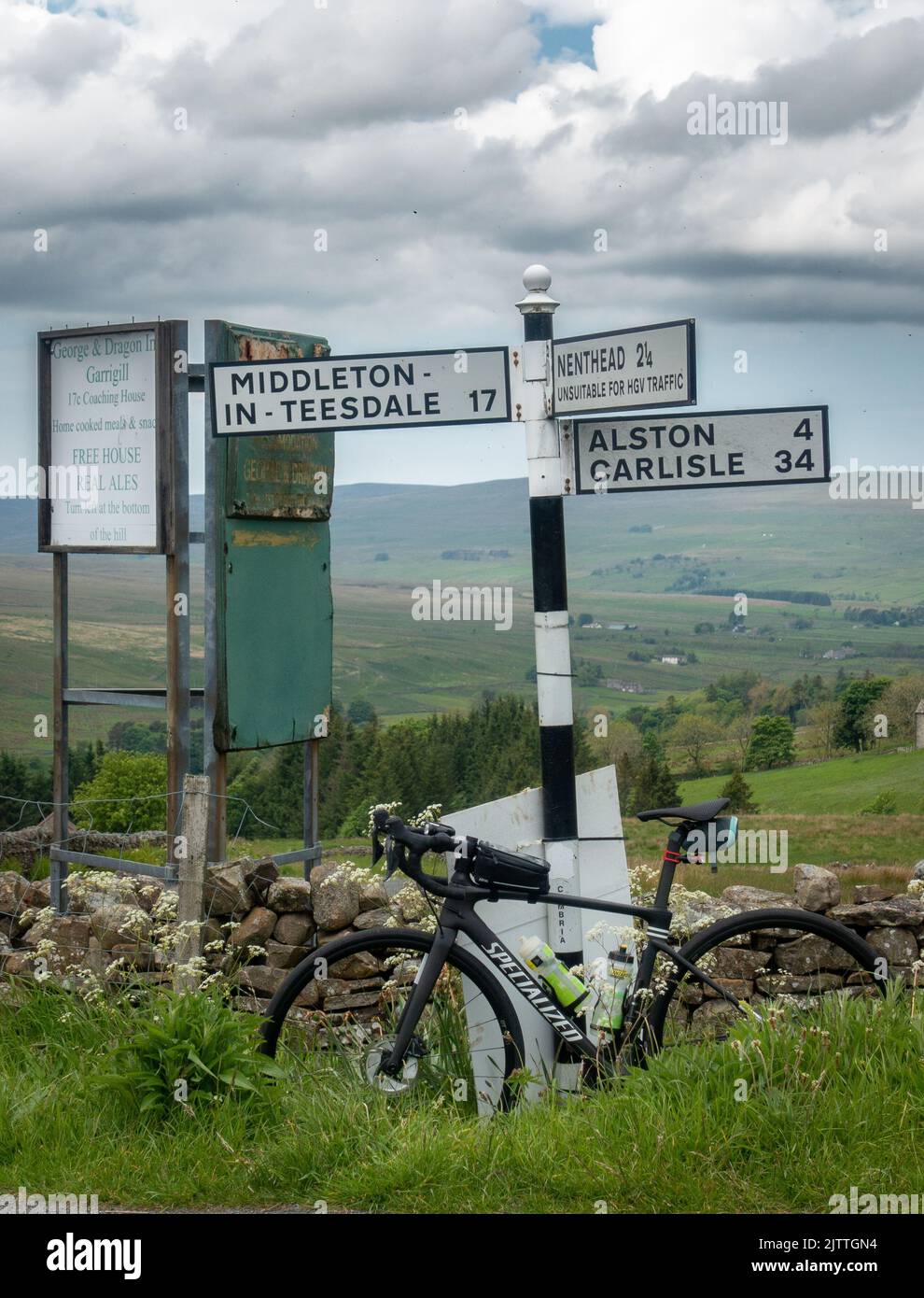Set di segnaletica tradizionale vicino a Garrigill con una bici da strada appoggiata al posto, segnaletica Middleton-in-Teesdale, Alston, Carlisle e Nent Foto Stock