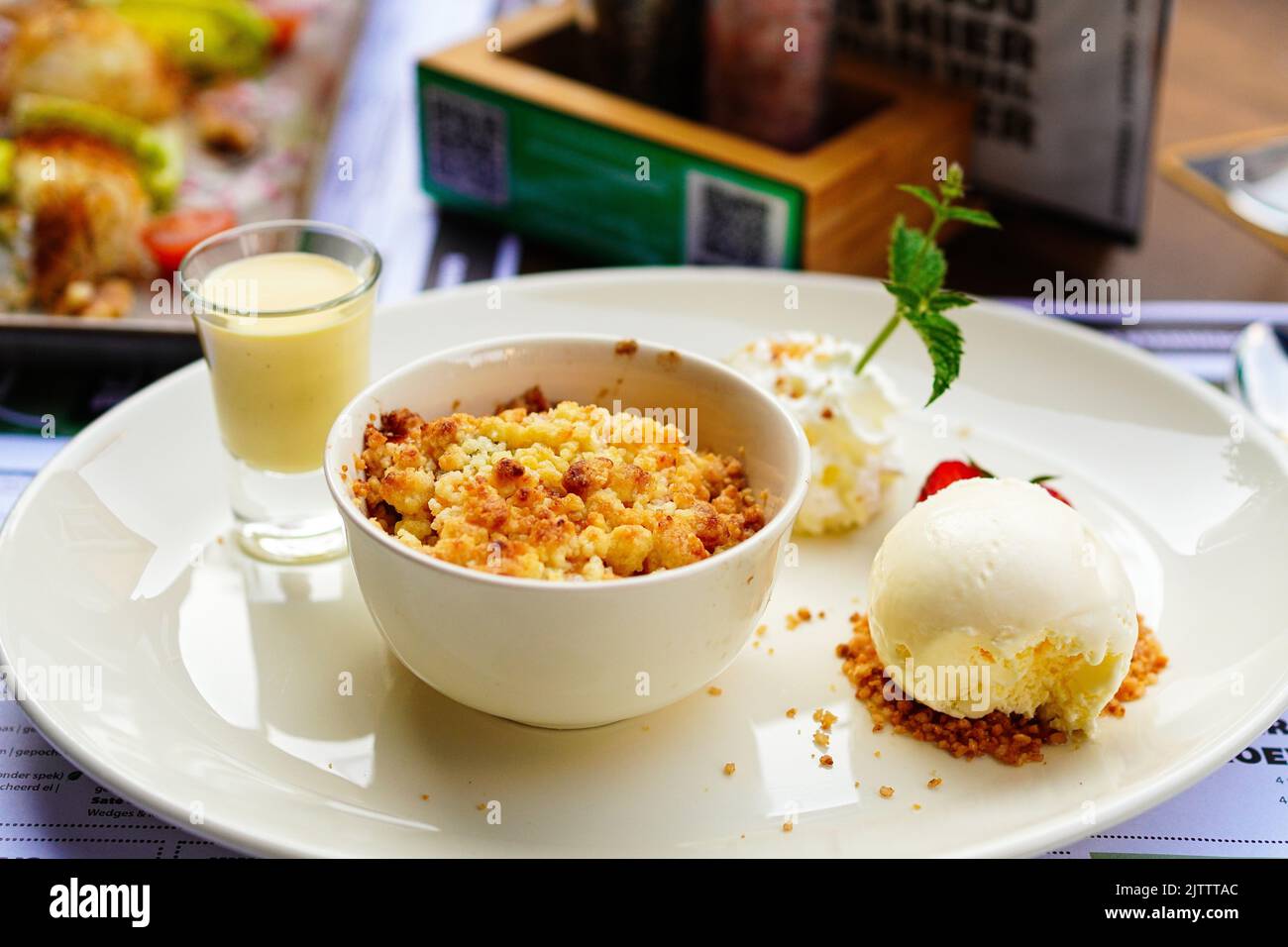 Crumble di mele fatto in casa con gelato alla vaniglia, fragola e crema pasticcera sul tavolo Foto Stock