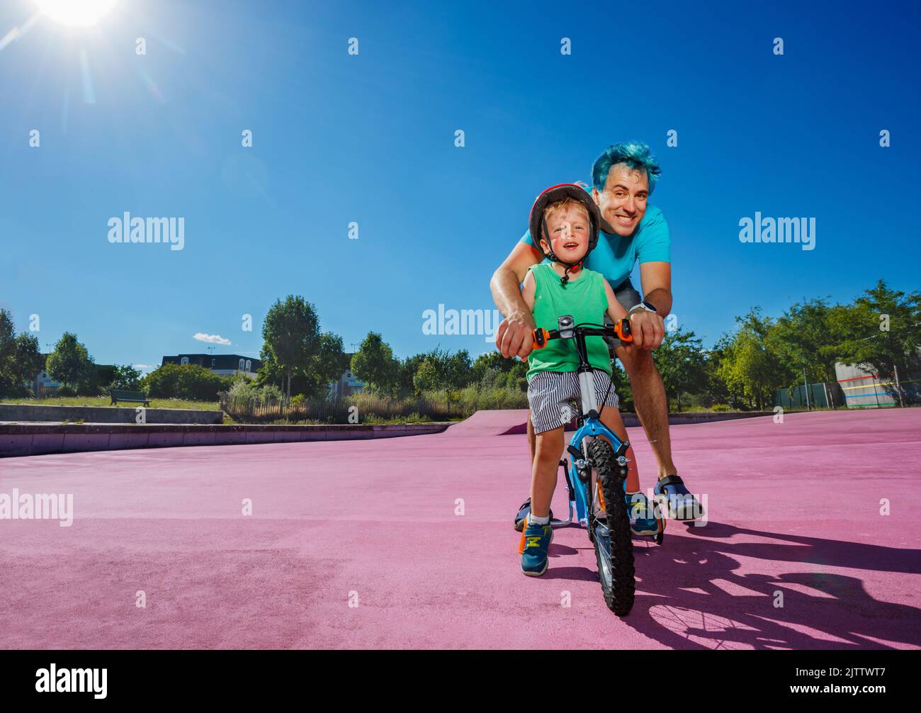 Padre con i capelli blu aiuta il bambino a imparare a guidare una bicicletta Foto Stock