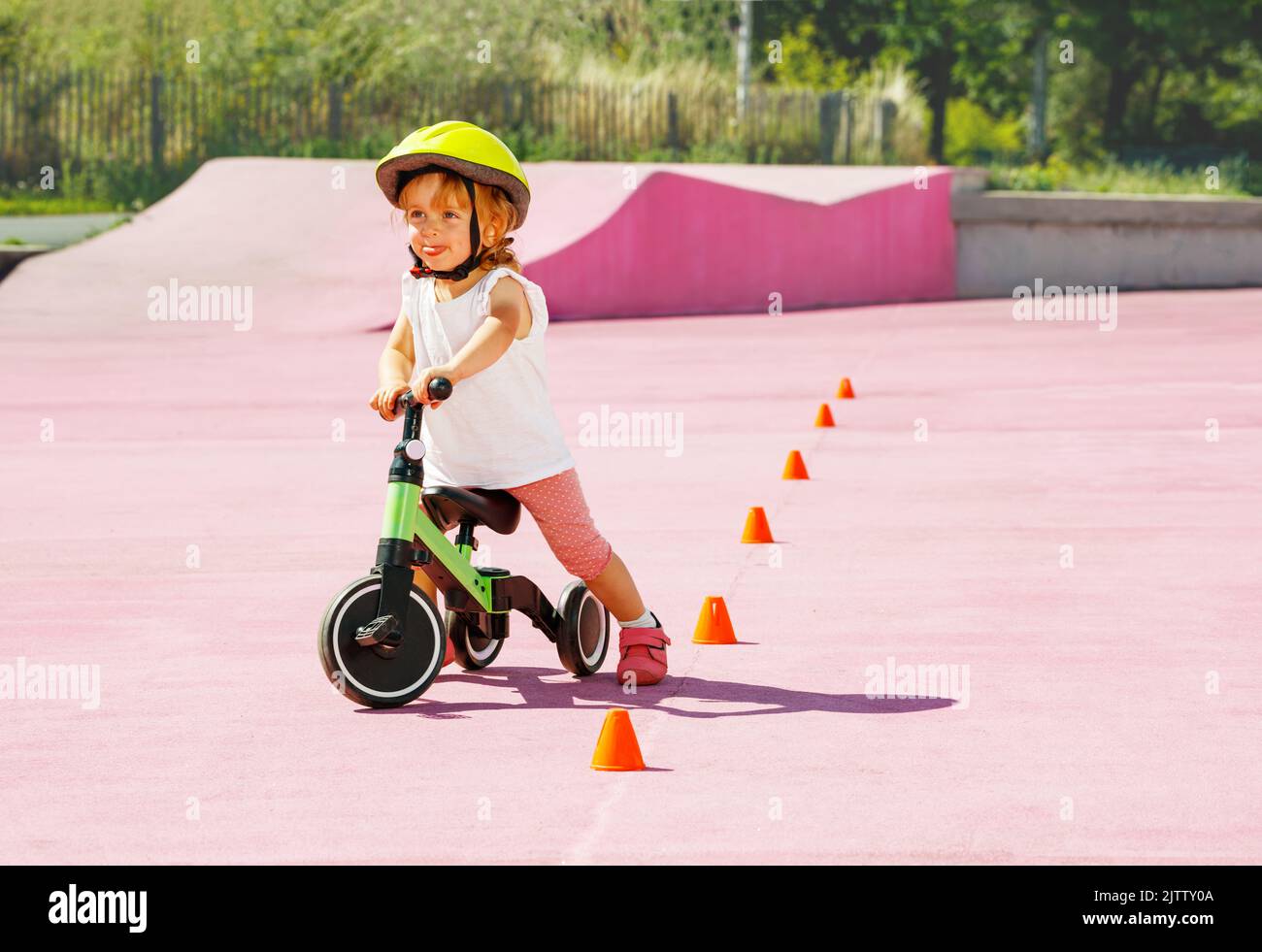 Baby girl cavalca una piccola bicicletta a tre ruote intorno ai coni arancioni Foto Stock