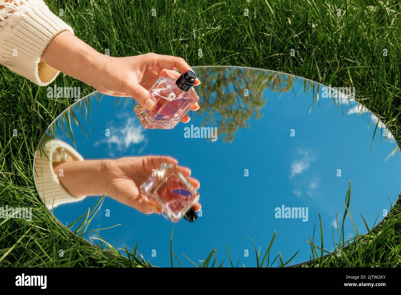 mano con profumo e riflesso del cielo in specchio Foto Stock