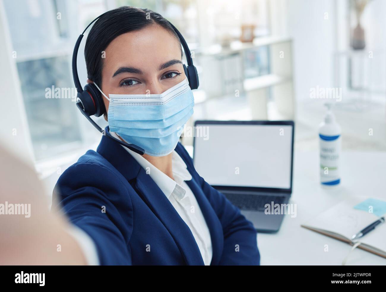 Assistenza clienti donna che prende selfie durante il lavoro al telefono mentre lavora su laptop e maschera facciale. L'addetto alla reception o l'agente del call center scattano una foto Foto Stock