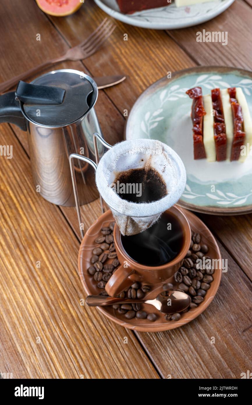 Pulire il filtro del caffè sulla tazza e sui chicchi di caffè. Sullo sfondo, guava dolce e formaggio cagliato. Foto Stock