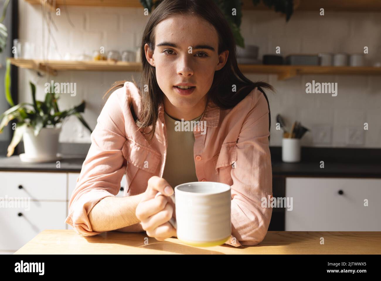 Ritratto di donna trans non binaria che tiene una tazza di caffè in cucina a casa Foto Stock