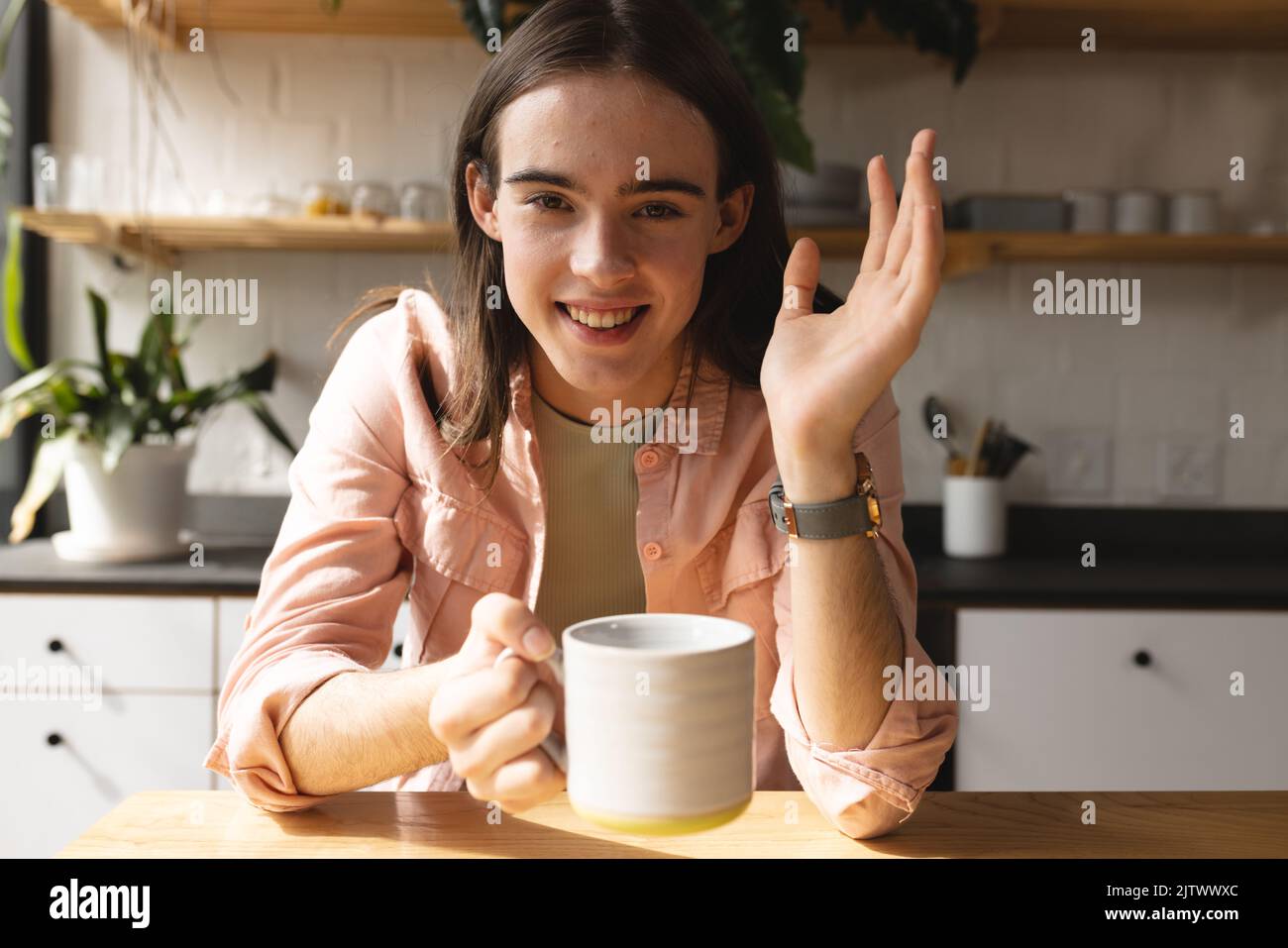 Ritratto di donna trans non binaria con caffè sorridente in cucina a casa Foto Stock